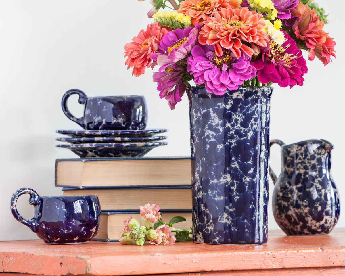 A stack of our classic dinnerware in customer favorite Blue Agate glaze.  A dark blue speckled on a tan base color, each piece hand glazed and no two alike. Lunch and Dinner plates shown along with medium basic bowls.  The tall utensil crock is in the background, doubling as a vase here with bright foliage for the season.